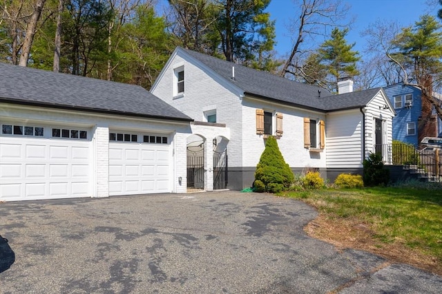 view of front facade with a garage, a chimney, brick siding, and aphalt driveway