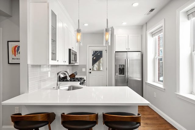 kitchen featuring stainless steel appliances, visible vents, backsplash, a sink, and a peninsula