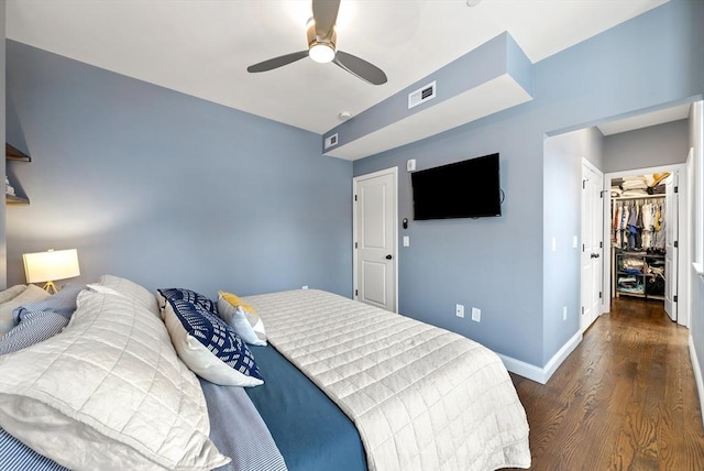 bedroom featuring ceiling fan, wood finished floors, visible vents, baseboards, and a spacious closet