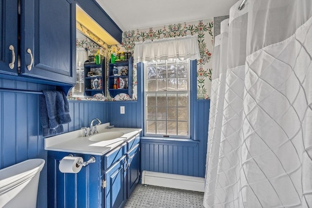 interior space with wallpapered walls, wainscoting, toilet, vanity, and a baseboard heating unit