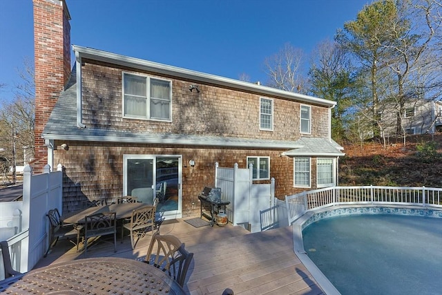 rear view of house with outdoor dining area, a chimney, and a wooden deck