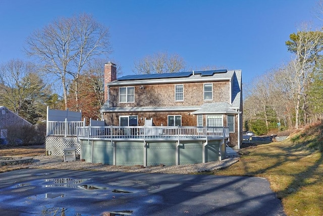 rear view of property featuring roof mounted solar panels, a chimney, a deck, and a lawn