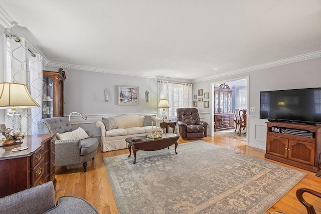 living area with a wainscoted wall, light wood-style flooring, ornamental molding, and a decorative wall