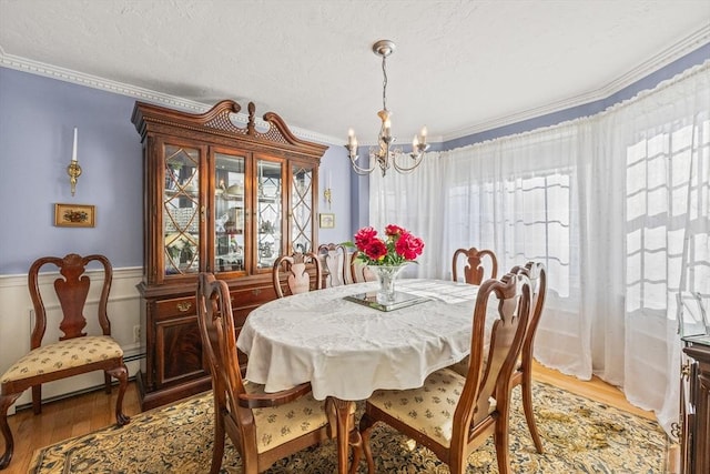 dining space featuring a textured ceiling, light wood-style flooring, a notable chandelier, ornamental molding, and baseboard heating