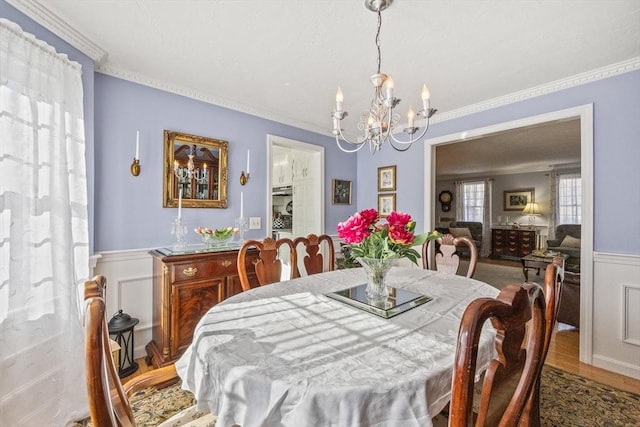 dining area featuring ornamental molding, wainscoting, an inviting chandelier, and wood finished floors