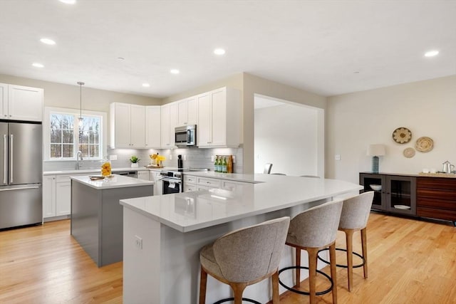 53 Driftwood Cir Unit 20, Sandown, NH 03873 - kitchen featuring appliances with stainless steel finishes, a kitchen island, a breakfast bar area, decorative backsplash, and light wood-type flooring