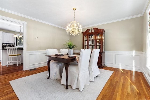 dining area with crown molding, a notable chandelier, and light wood-type flooring