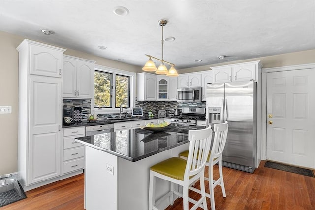 kitchen with dark hardwood / wood-style flooring, a kitchen island, pendant lighting, stainless steel appliances, and white cabinets