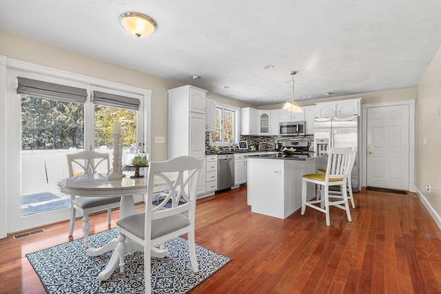 kitchen with dark wood-type flooring, white cabinetry, backsplash, stainless steel appliances, and decorative light fixtures