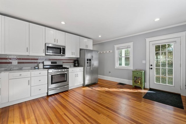 kitchen featuring appliances with stainless steel finishes, crown molding, decorative backsplash, white cabinets, and light wood-type flooring