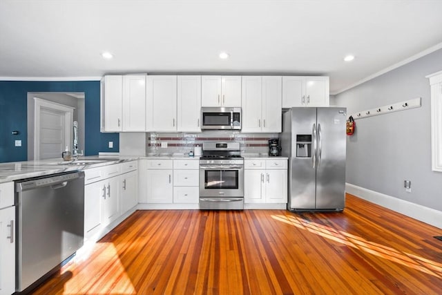 kitchen featuring white cabinetry, stainless steel appliances, crown molding, hardwood / wood-style floors, and decorative backsplash