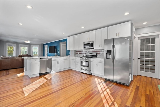 kitchen with kitchen peninsula, light hardwood / wood-style flooring, white cabinets, and appliances with stainless steel finishes