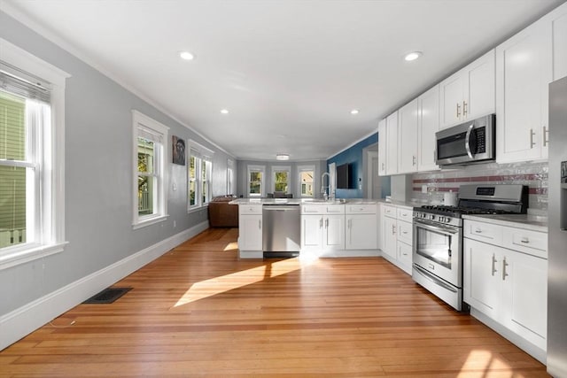 kitchen with white cabinets, kitchen peninsula, crown molding, and appliances with stainless steel finishes