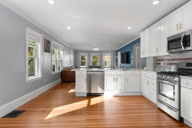 kitchen featuring white cabinetry, sink, kitchen peninsula, crown molding, and appliances with stainless steel finishes