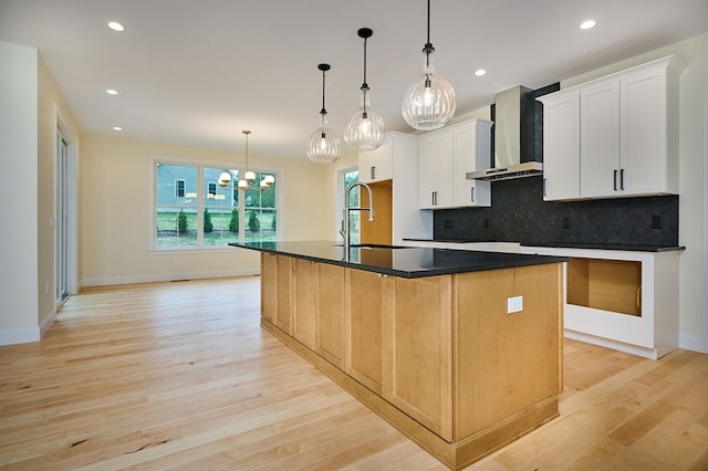 kitchen with a kitchen island with sink, white cabinetry, light hardwood / wood-style flooring, tasteful backsplash, and wall chimney exhaust hood