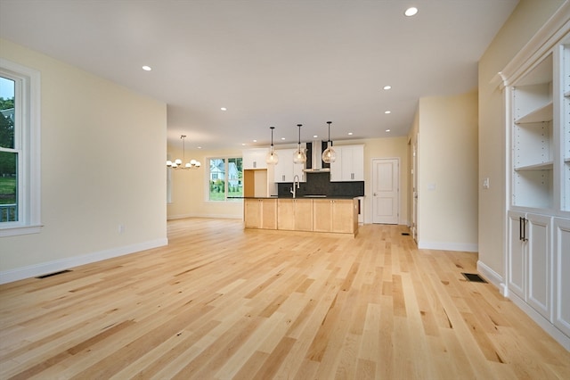 unfurnished living room featuring a notable chandelier and light hardwood / wood-style floors