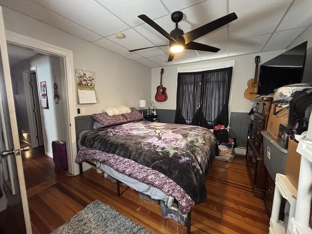 bedroom with a drop ceiling, a baseboard heating unit, ceiling fan, and wood finished floors