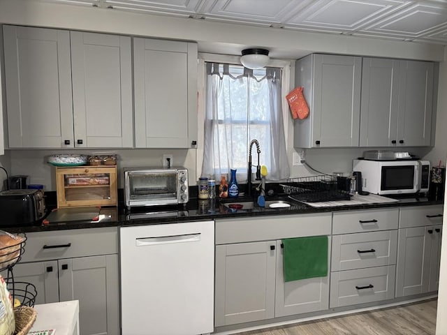 kitchen featuring light wood finished floors, a toaster, dark stone counters, white appliances, and a sink