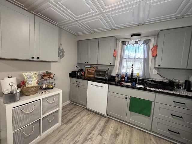 kitchen featuring light wood finished floors, a toaster, dishwasher, gray cabinets, and an ornate ceiling