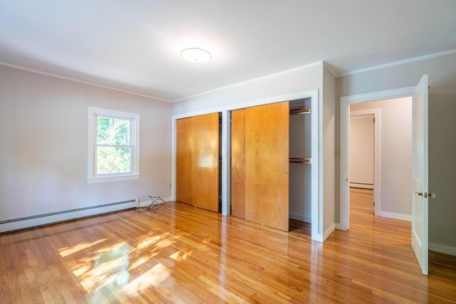 unfurnished bedroom featuring ornamental molding, hardwood / wood-style flooring, baseboard heating, and multiple closets