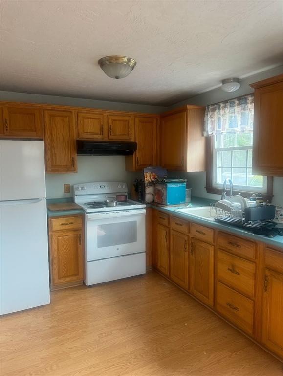 kitchen with white appliances, light wood-style floors, brown cabinets, under cabinet range hood, and a sink