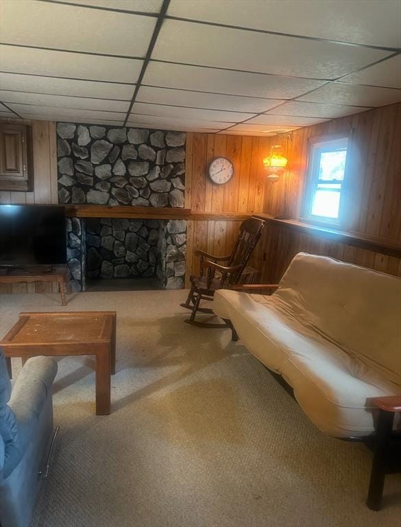 living area with a paneled ceiling, carpet, wooden walls, and a stone fireplace