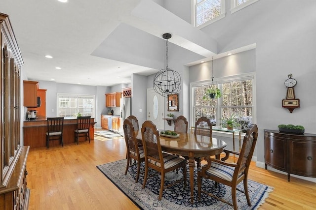 dining area with a notable chandelier, a towering ceiling, plenty of natural light, and light wood-type flooring