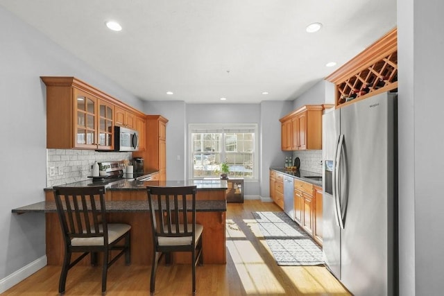 kitchen featuring light wood-type flooring, appliances with stainless steel finishes, a kitchen breakfast bar, kitchen peninsula, and decorative backsplash