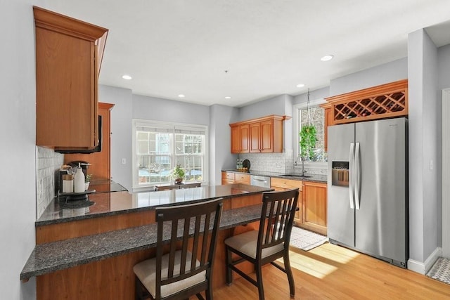 kitchen with sink, stainless steel fridge with ice dispenser, light wood-type flooring, a kitchen breakfast bar, and backsplash