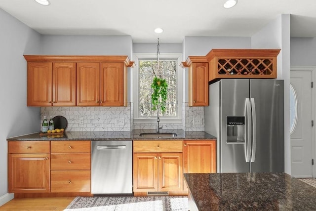 kitchen with sink, tasteful backsplash, light hardwood / wood-style flooring, dark stone countertops, and stainless steel appliances