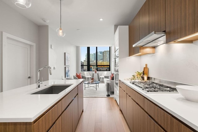 kitchen with a sink, light countertops, appliances with stainless steel finishes, wall chimney exhaust hood, and decorative light fixtures