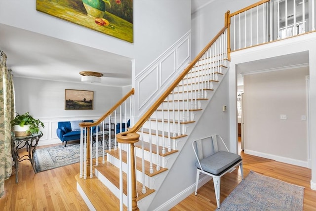 stairway with ornamental molding, a high ceiling, baseboards, and wood finished floors