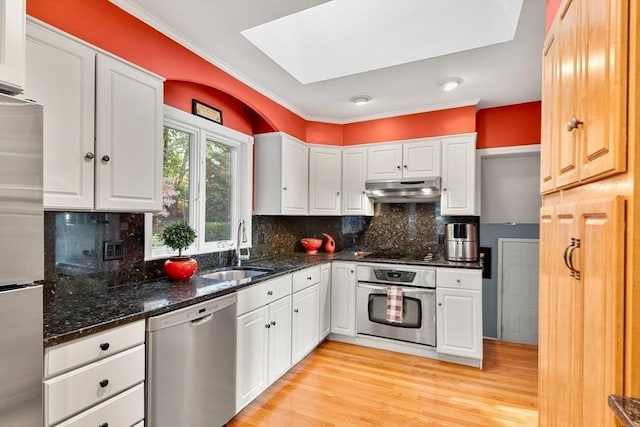 kitchen with appliances with stainless steel finishes, a skylight, under cabinet range hood, a sink, and white cabinets