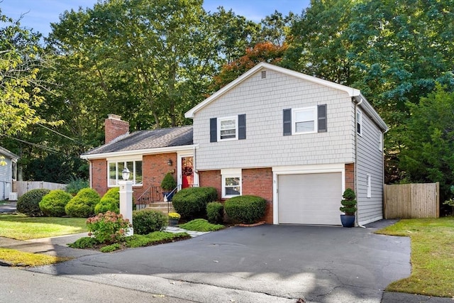 tri-level home featuring fence, brick siding, a chimney, a garage, and driveway