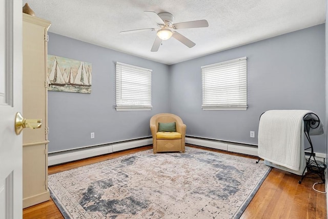 living area with a baseboard heating unit, ceiling fan, wood finished floors, and a textured ceiling