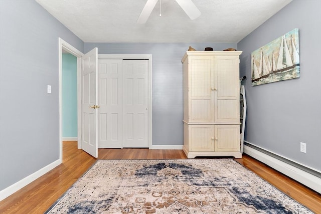 unfurnished bedroom with a baseboard heating unit, light wood-type flooring, a closet, baseboards, and ceiling fan