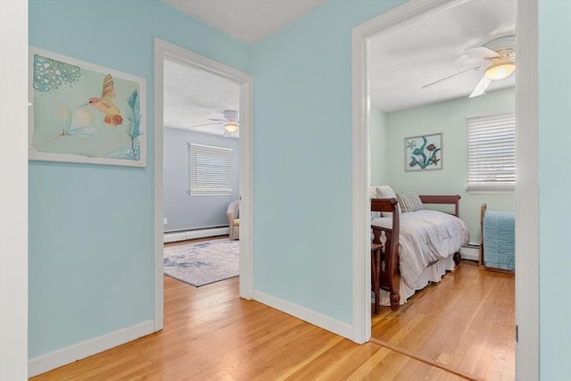 hall featuring baseboard heating, wood finished floors, baseboards, and a baseboard radiator