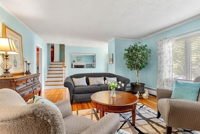living area with ornamental molding, wood finished floors, a baseboard radiator, stairway, and a textured ceiling