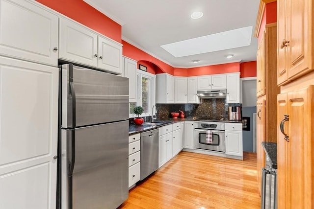 kitchen featuring appliances with stainless steel finishes, under cabinet range hood, a sink, a skylight, and white cabinets