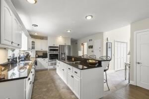 5 Lancaster Ln, Bourne, MA 02532 - kitchen featuring a breakfast bar area, stainless steel appliances, white cabinetry, dark countertops, and a kitchen island