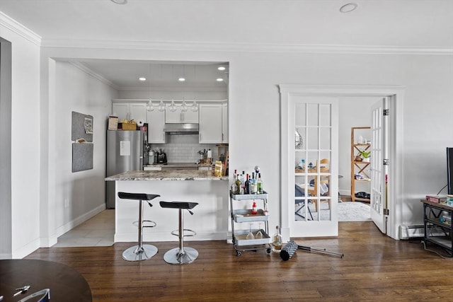 kitchen with decorative backsplash, a breakfast bar, wood finished floors, freestanding refrigerator, and under cabinet range hood