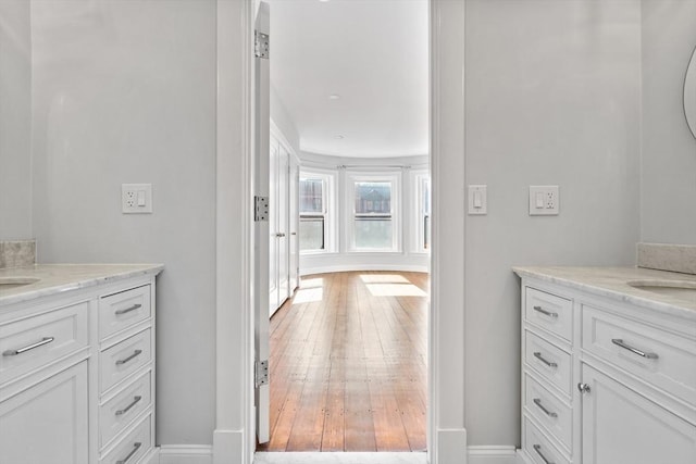 bathroom featuring baseboards, two vanities, and wood finished floors