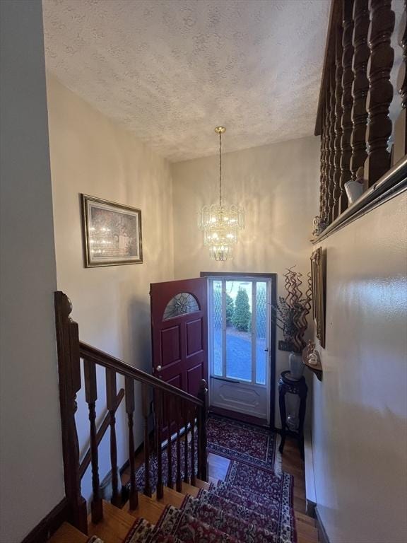 foyer entrance with stairs, wood finished floors, baseboards, a textured ceiling, and a notable chandelier