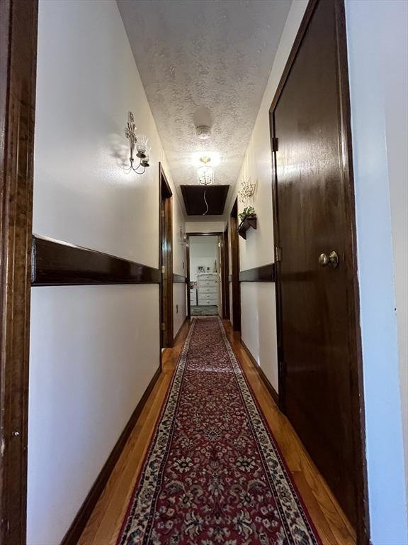 hall featuring baseboards, a textured ceiling, wood finished floors, and attic access