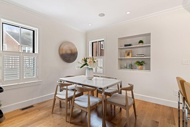 dining area featuring light wood finished floors, plenty of natural light, visible vents, and ornamental molding