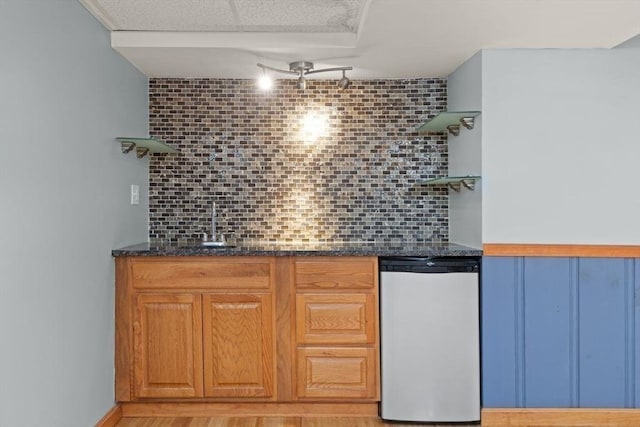 bar featuring stainless steel dishwasher, sink, decorative backsplash, and light wood-type flooring