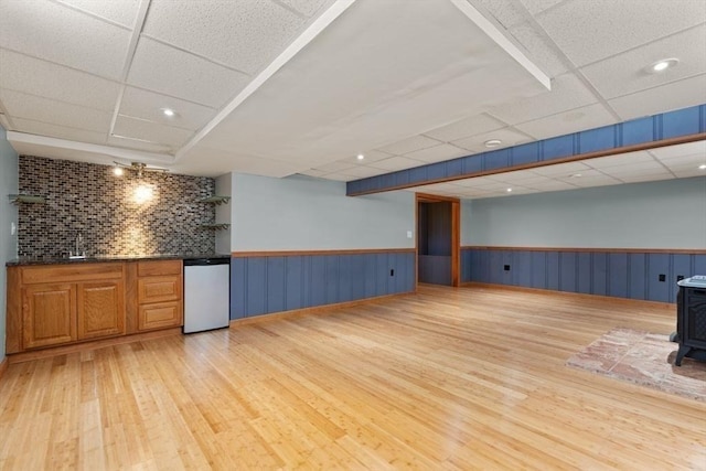 interior space featuring a wood stove, wet bar, a drop ceiling, and light wood-type flooring