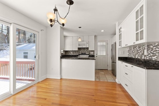 kitchen with appliances with stainless steel finishes, hanging light fixtures, white cabinets, decorative backsplash, and light wood-type flooring