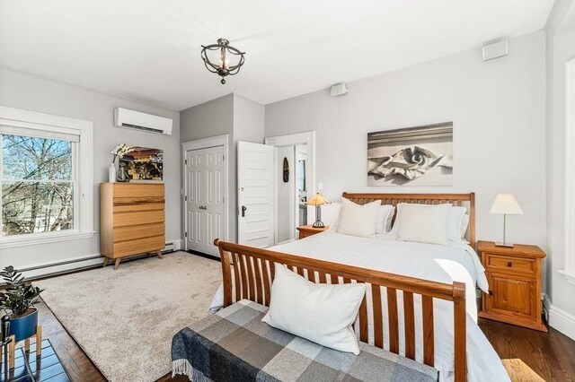 bedroom with a closet, an AC wall unit, baseboards, and wood finished floors