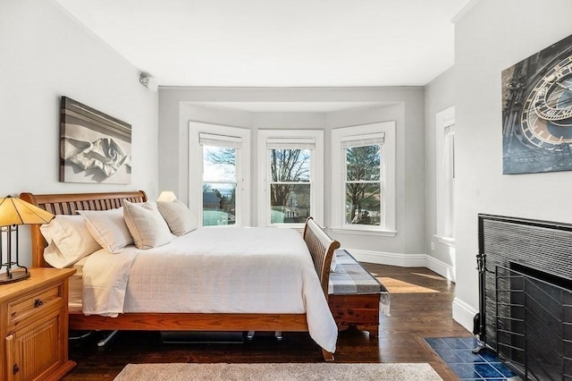 bedroom with dark wood finished floors, a fireplace, and baseboards